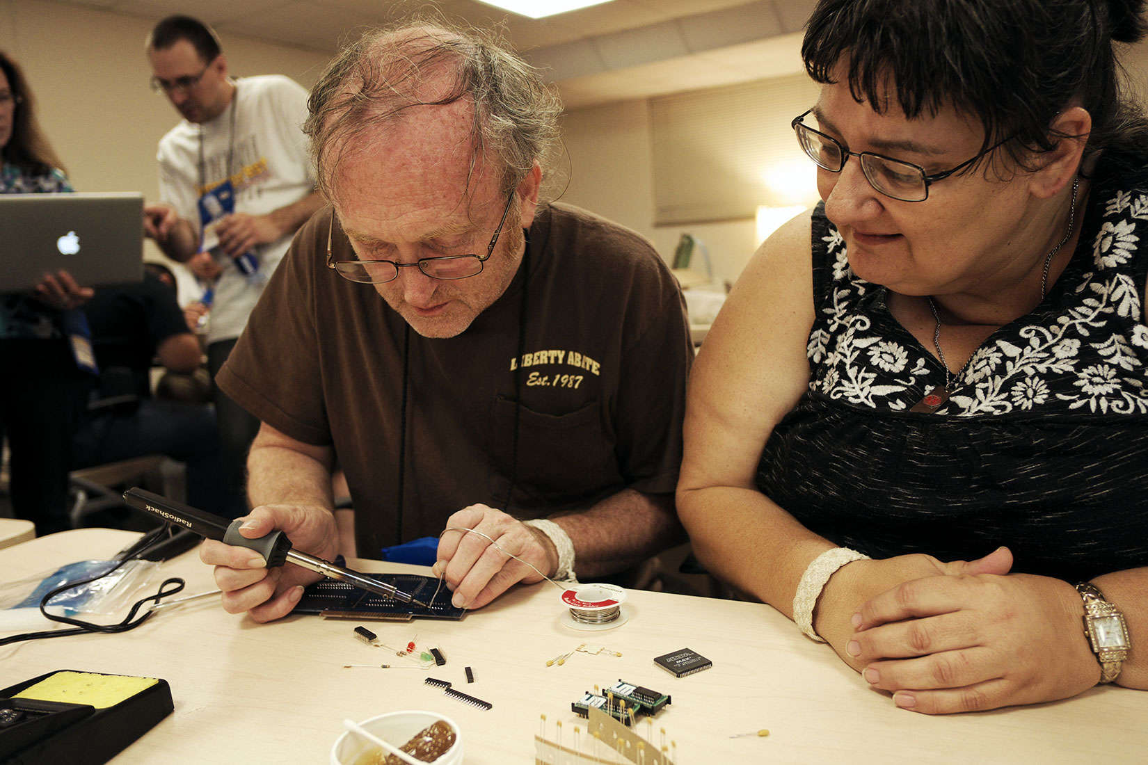 Rachele Lane watches her husband, John, try his hand at soldering at KansasFest.