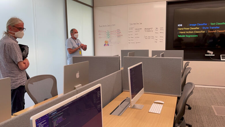 The tour of the Apple Developer Center starts in the hardware testing room. This room lets developers test their apps on devices they might not own, like Apple Watch. This room has a TV screen and cubicles with 24 iMacs.