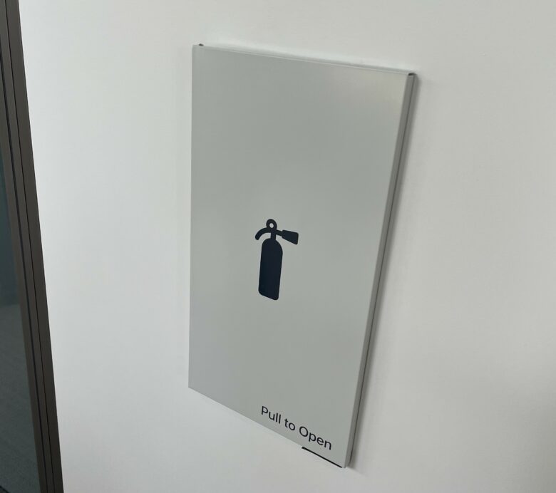 The fire extinguishers at the Apple Developer Center are hidden behind a silver door marked with a black icon. It looks like an SF Symbol.