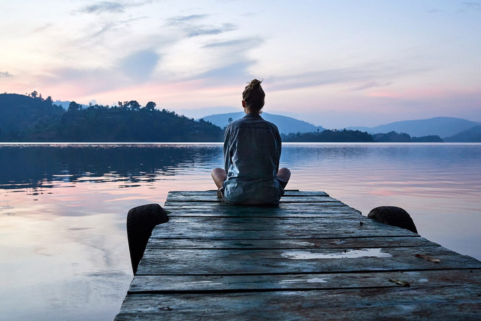 A woman meditating at the end of a boat dock at sunrise or sunset.