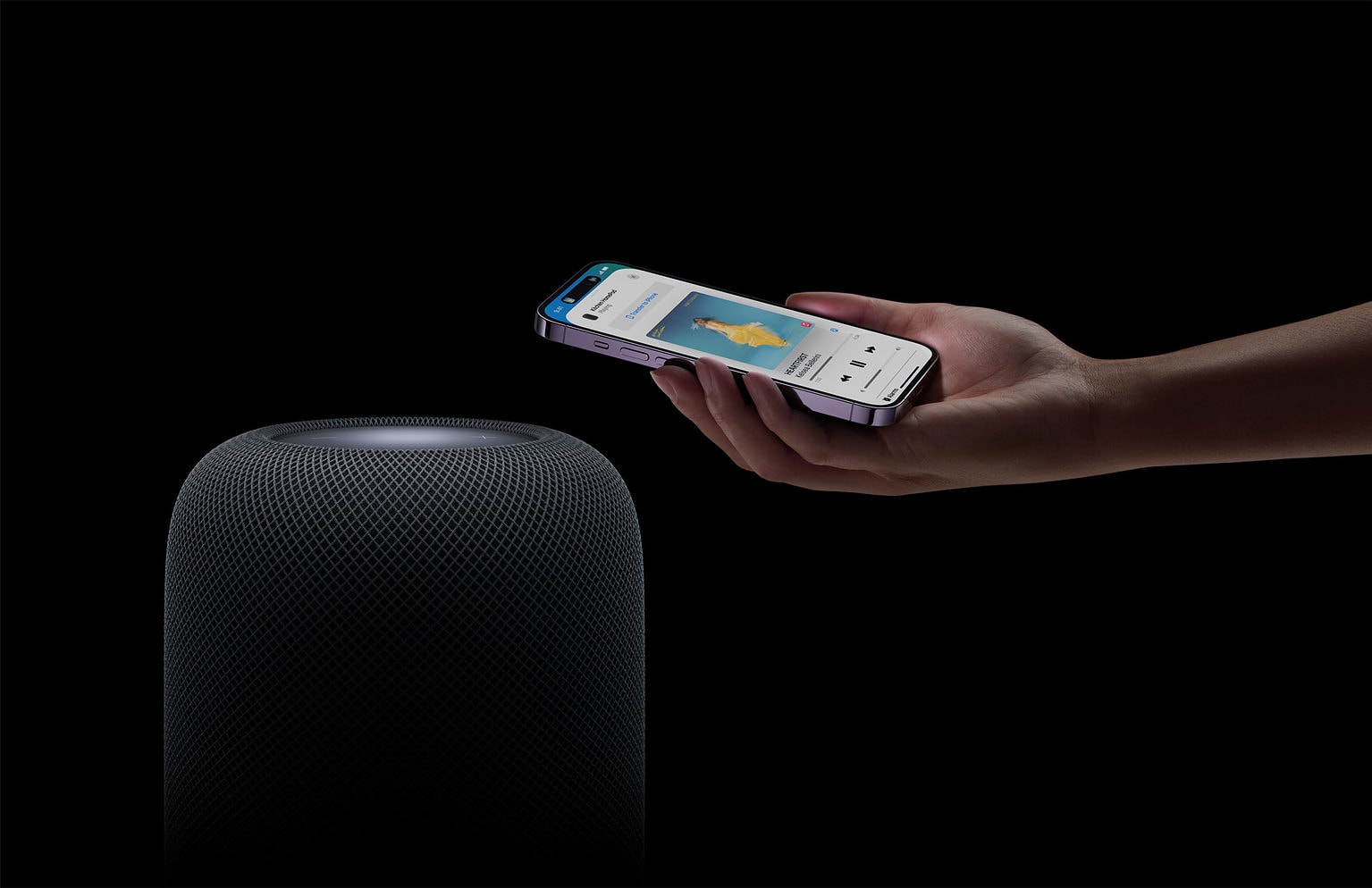 A second-generation HomePod and a hand holding an iPhone.
