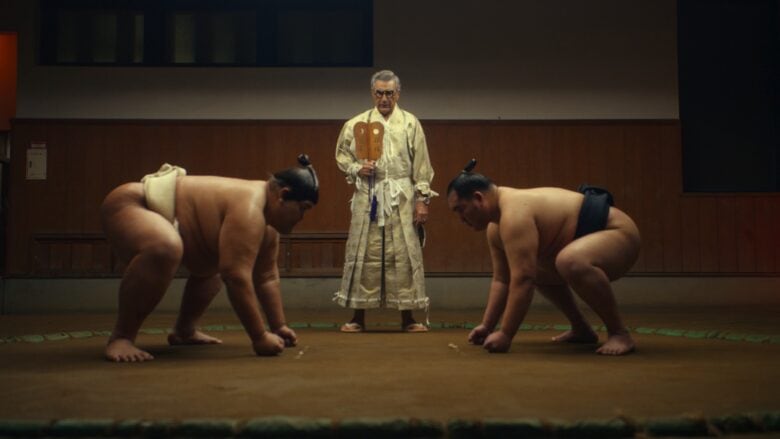 Eugene Levy watches two sumo wrestlers square off in the Tokyo episode of "The Reluctant Traveler" on Apple TV+.
