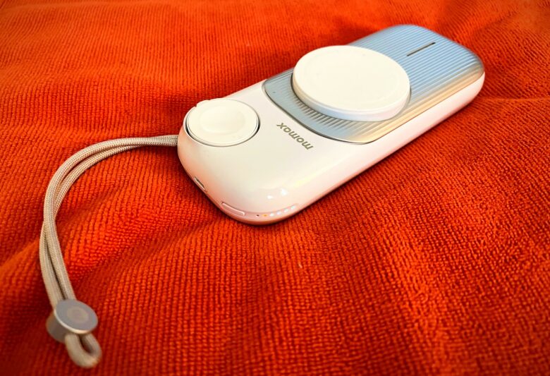 A product shot of Momax AirBox Go, a portable MagSafe power bank for iPhone, Apple Watch and AirPods, on a an orangish-red microfiber cloth.