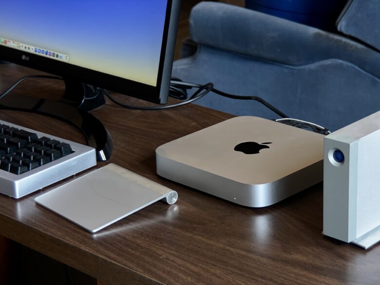 Mac mini sitting on desk alongside LG display, LaCie hard drive, Model F keyboard and Magic Trackpad
