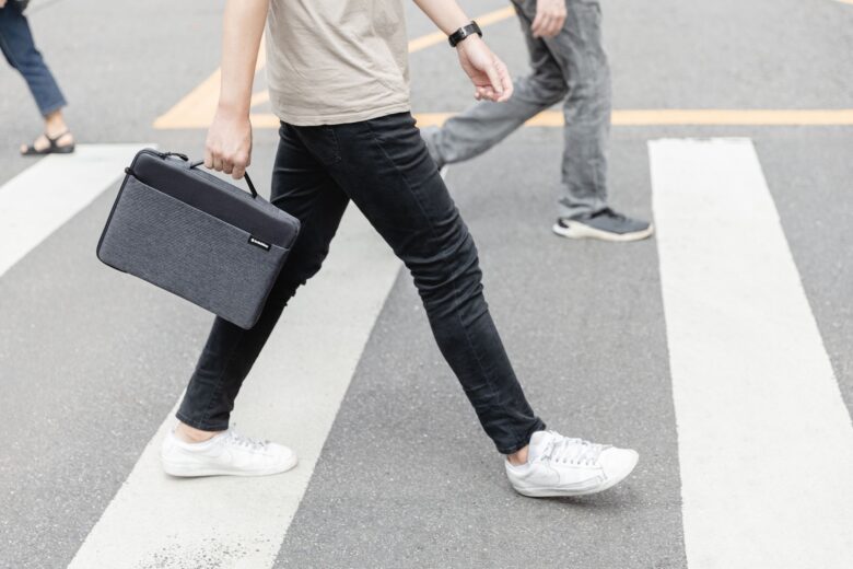 A pedestrian carries a SwitchEasy Urban MacBook Sleeve while walking in a crosswalk.
