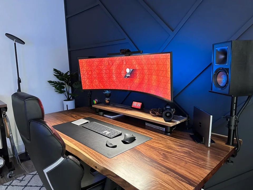 The accent wall and solid-wood DIY standing desk steal the show from the M2 MacBook Pro and 49-inch curved display.