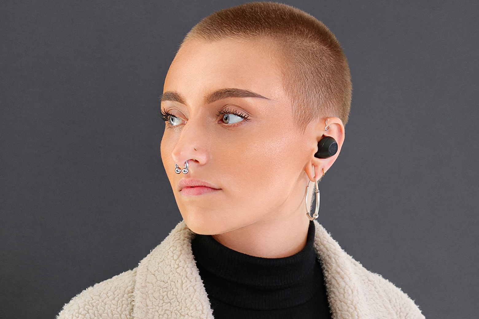 A woman with a shaved head wears Mymanu Clik S translation earbuds.