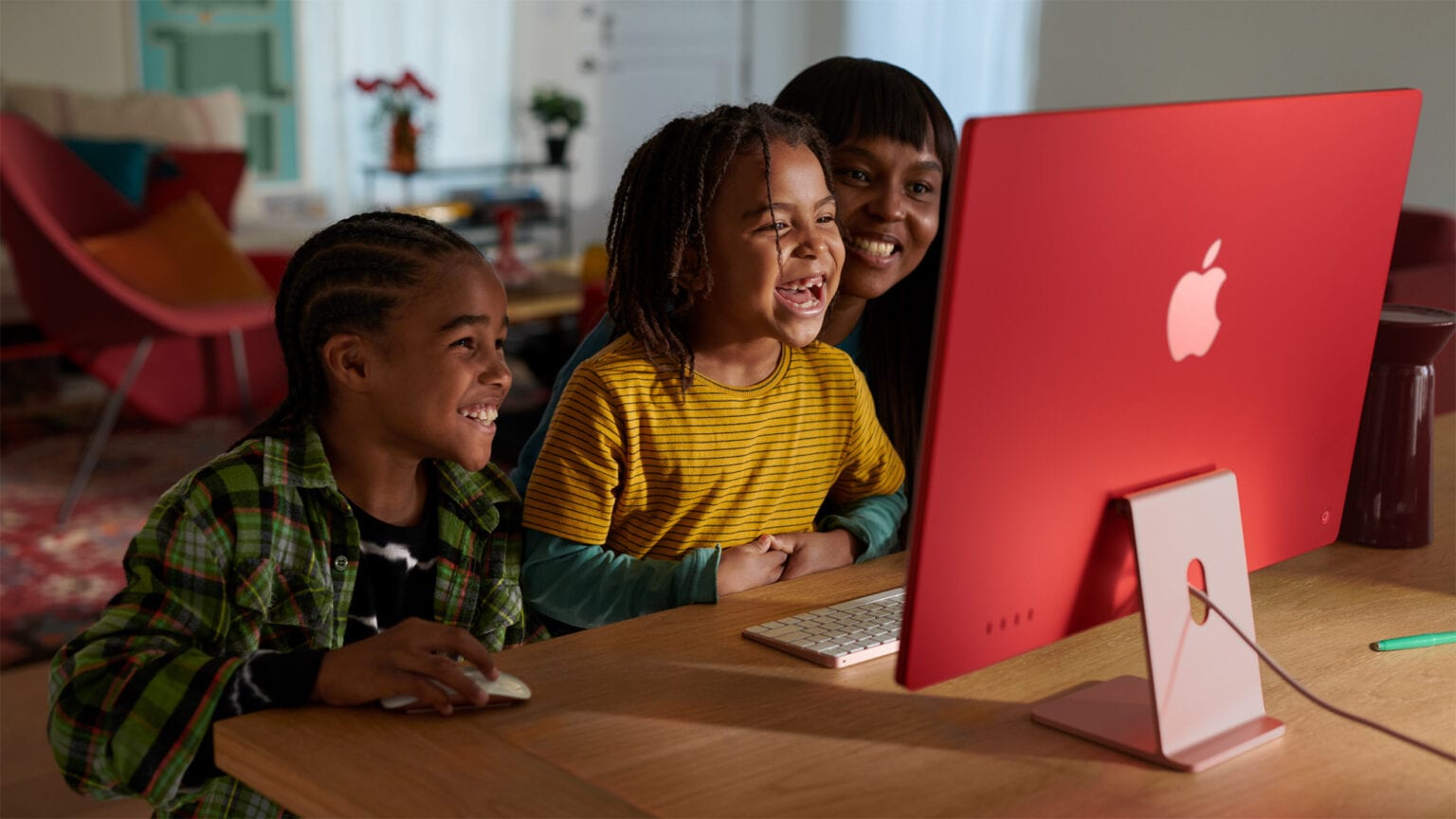 Three kids huddle in front of a red iMac powered by Apple's M3 chip.