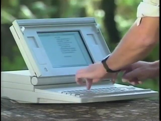 Macintosh Portable sitting on a rock in a forest, inexplicably