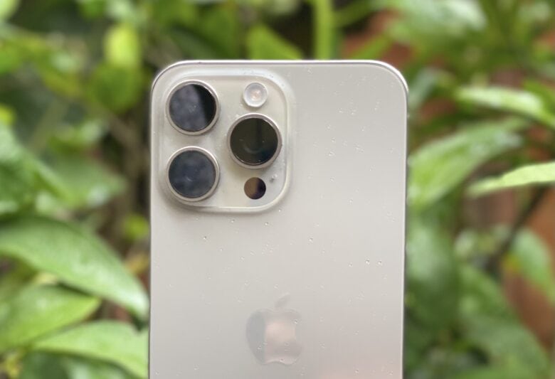 The iPhone 15 Pro Max camera array, pictured in front of a green plant.
