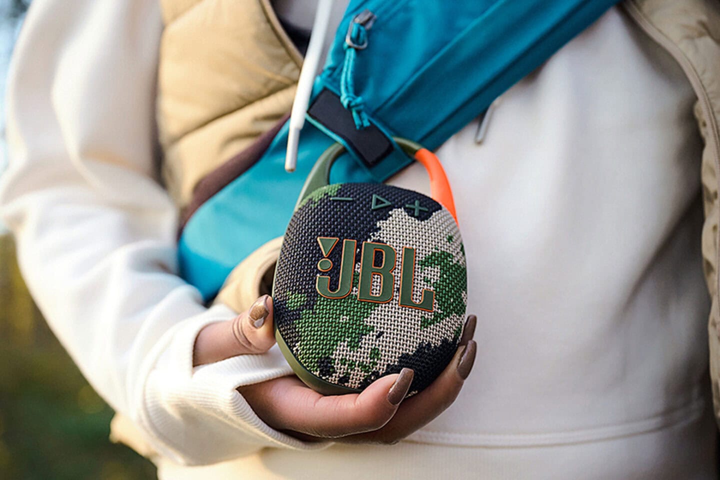Photo of a person holding a JBL Clip 5 ultra-portable Bluetooth speaker with built-in carabiner.