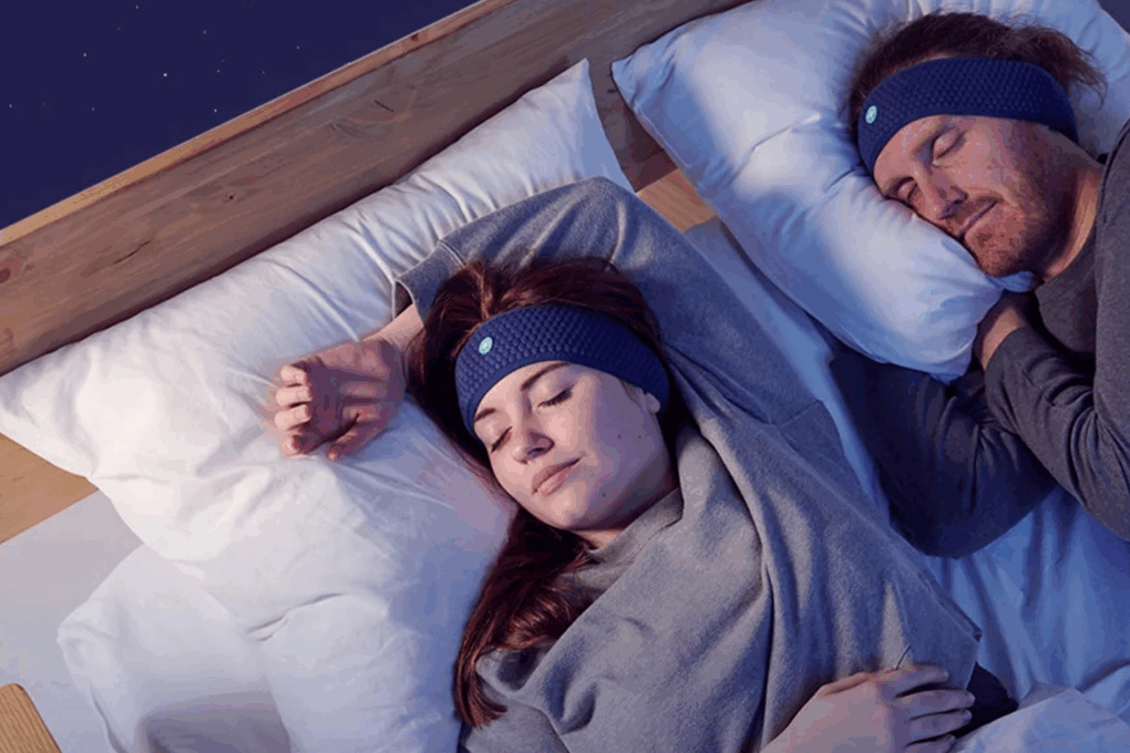 Man and woman asleep on the bed using sleep aids: HoomBands on their heads and Dodow slightly illuminating them.