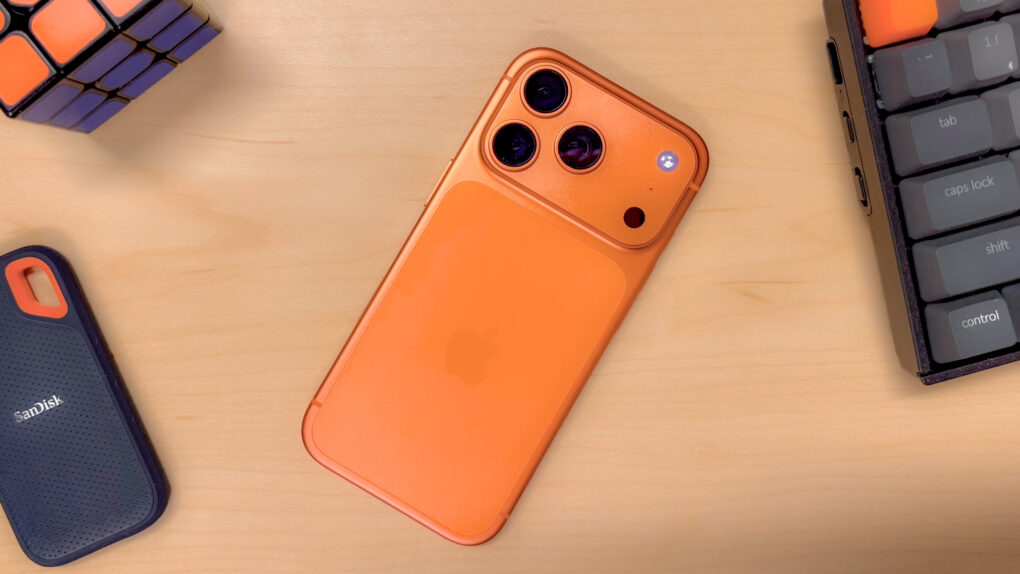 An iPhone 17 Pro in Cosmic Orange, on a desk surrounded by objects with orange accents