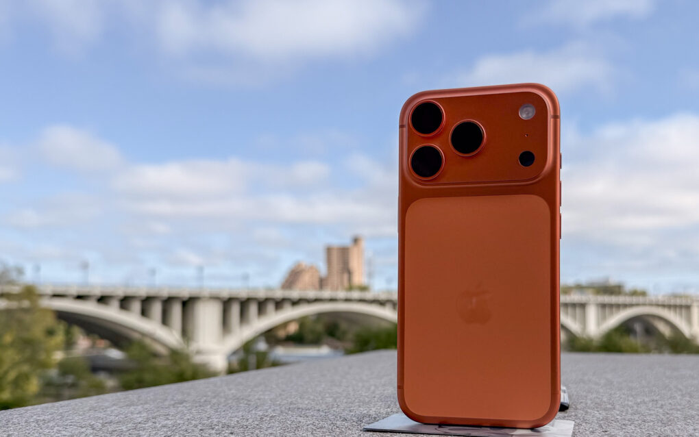 Cosmic Orange iPhone 17 Pro in front of a bridge with buildings in the distance