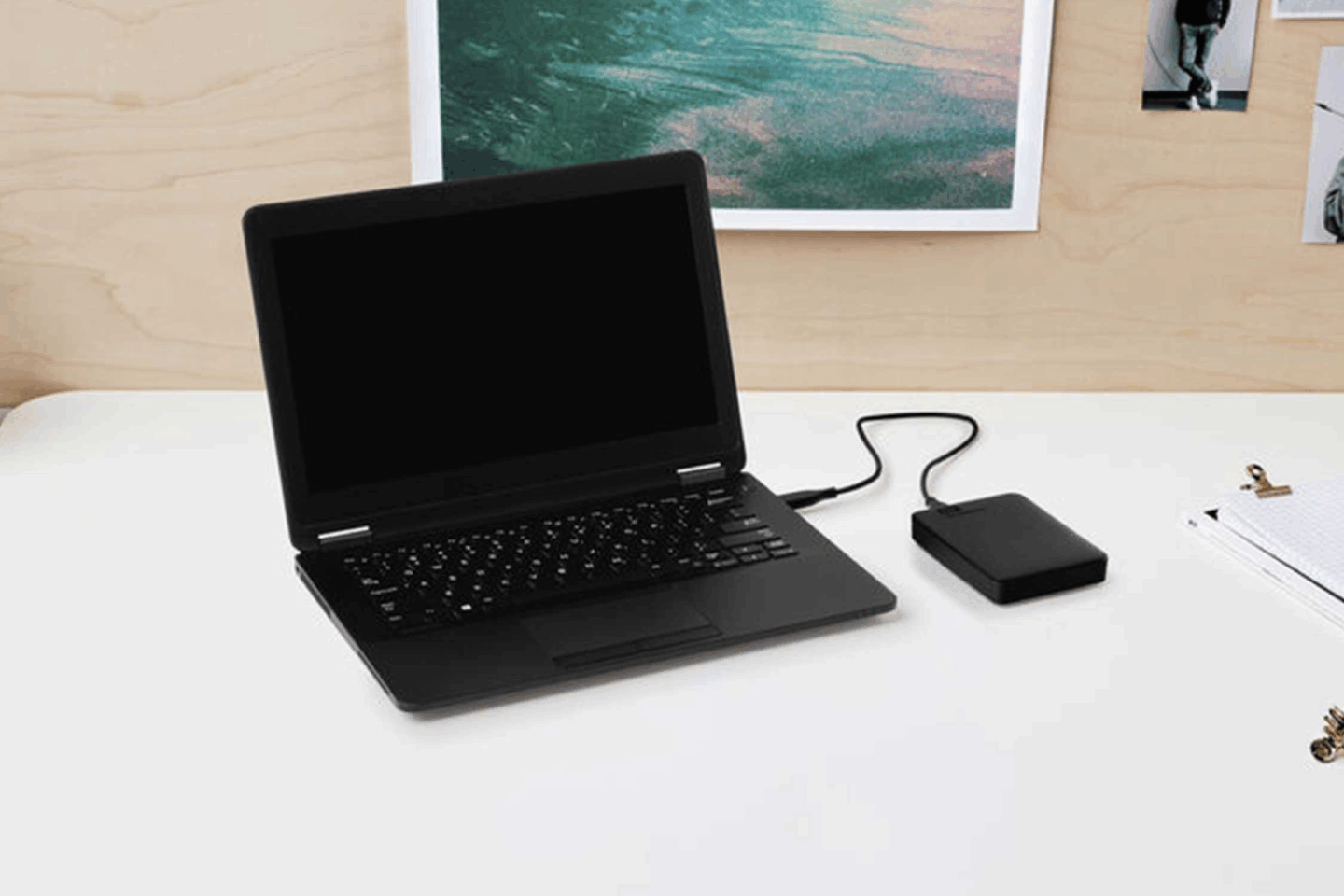 Photo of a black 2TB external hard drive connected to a black laptop on top of a white desk.