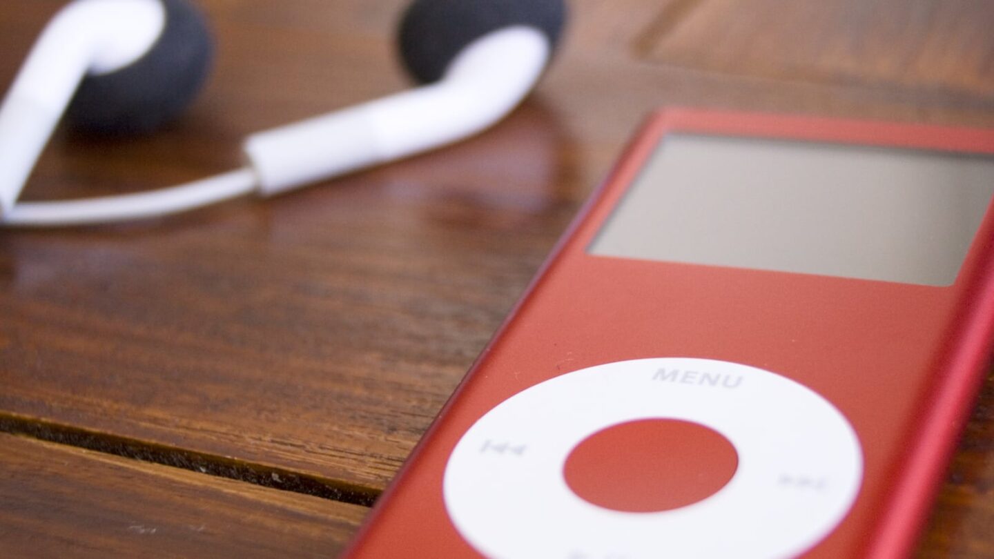 Photo of Product Red iPod nano sitting on wooden table with Apple EarPods in the background.