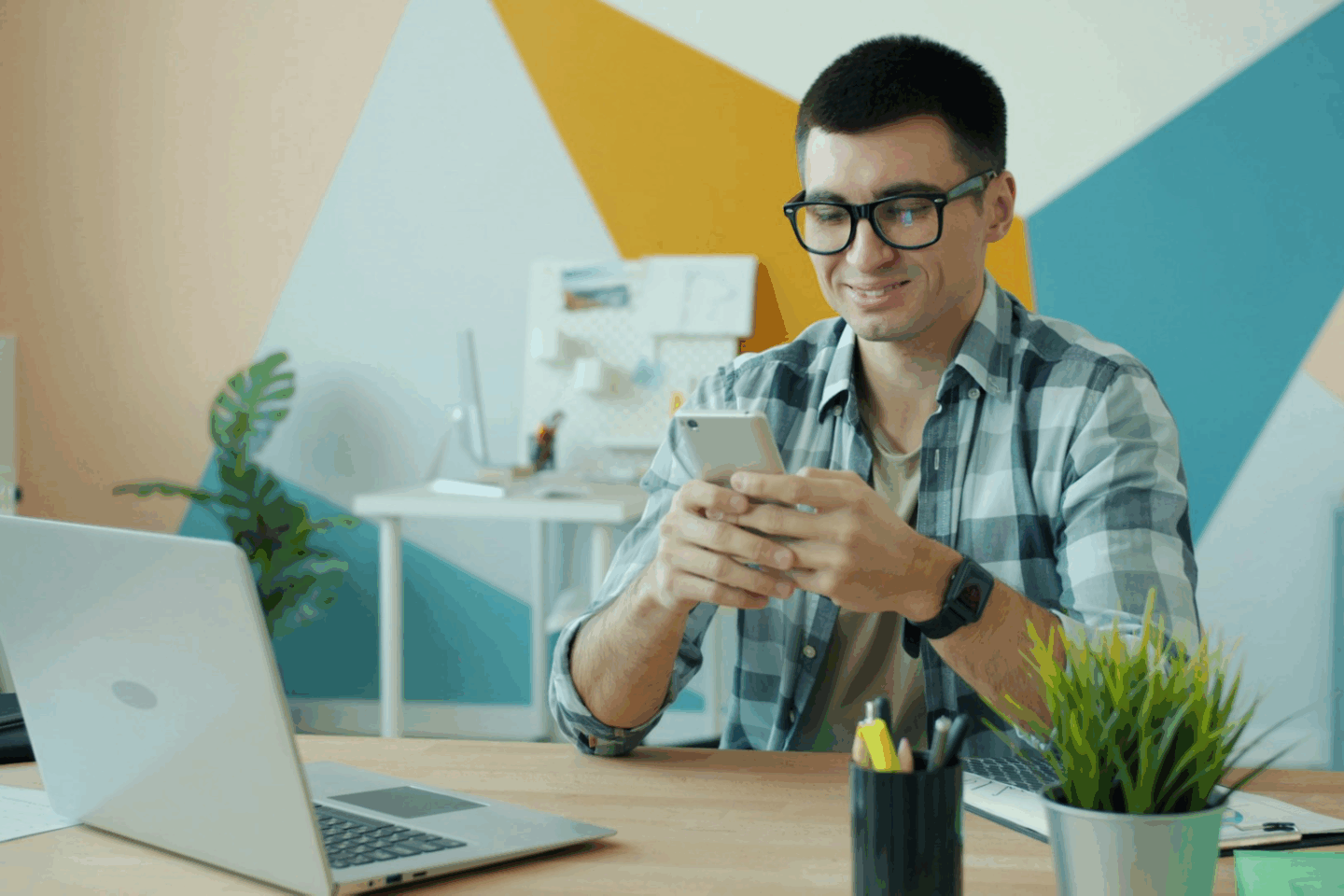 Man sitting in front of a work desk smiling at his phone as he learns how to make TikTok videos go viral using TikTokWizard Pro