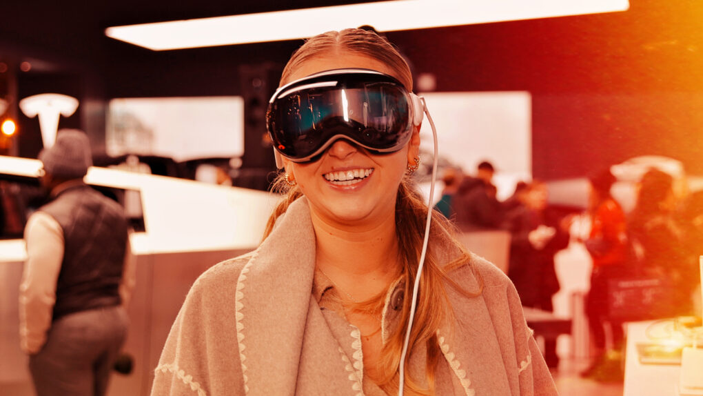 A digitally altered image of a woman wearing an Apple Vision Pro headset in a workplace environment.