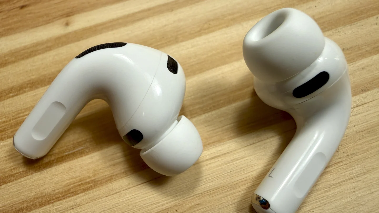 Closeup of the AirPods Pro 3, and their tips, on a pine table