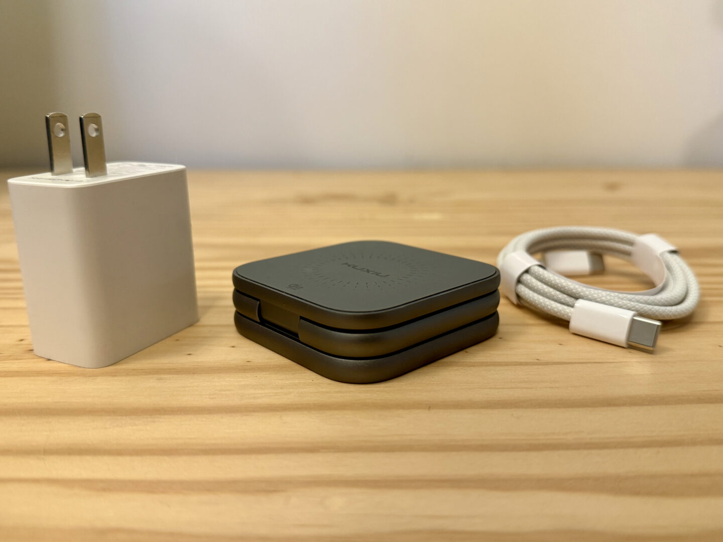 Kuxiu X40 Turbo sitting, folded up, on a pine table next to a power adapter and cable