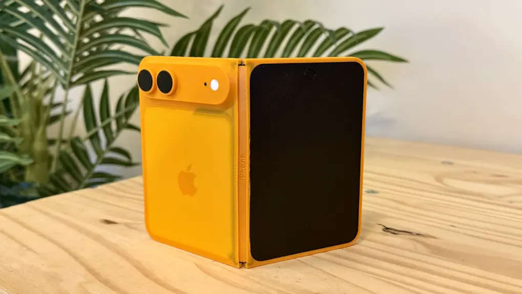Orange folding iPhone model sitting on a pine table in front of a fake palm tree