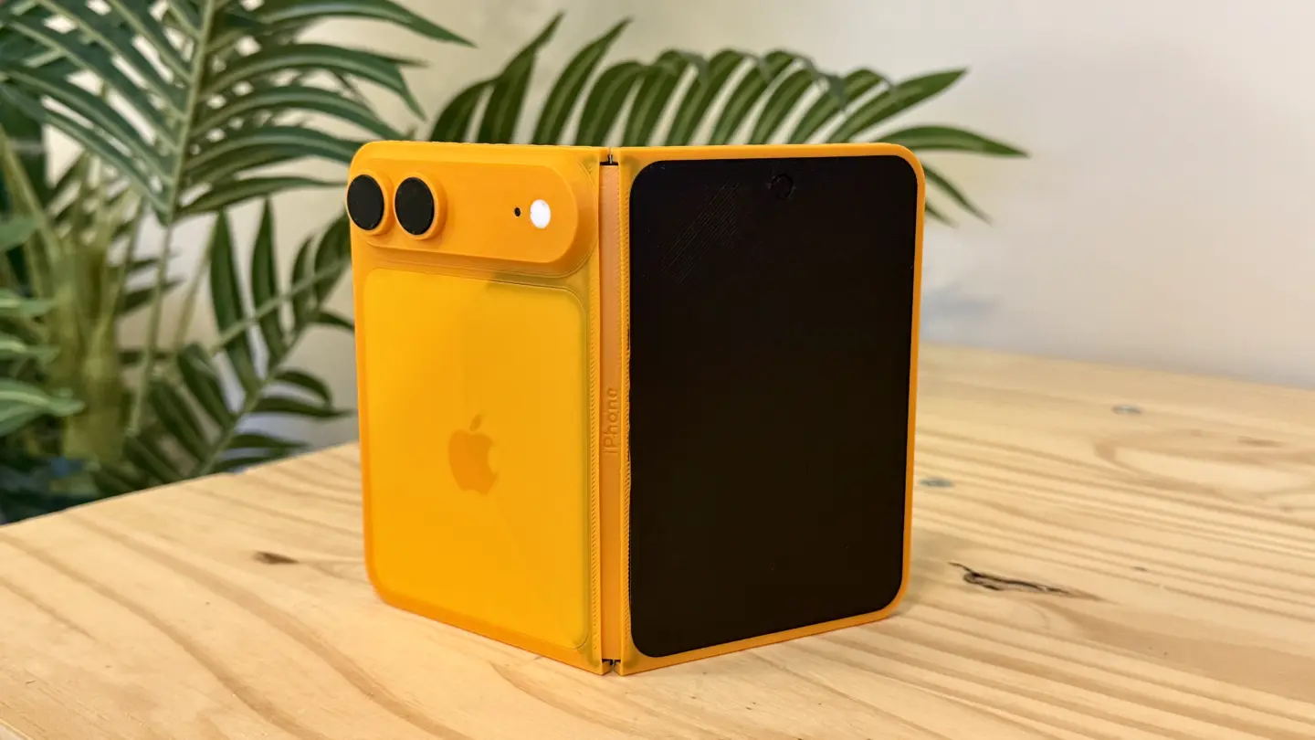 Orange folding iPhone model sitting on a pine table in front of a fake palm tree