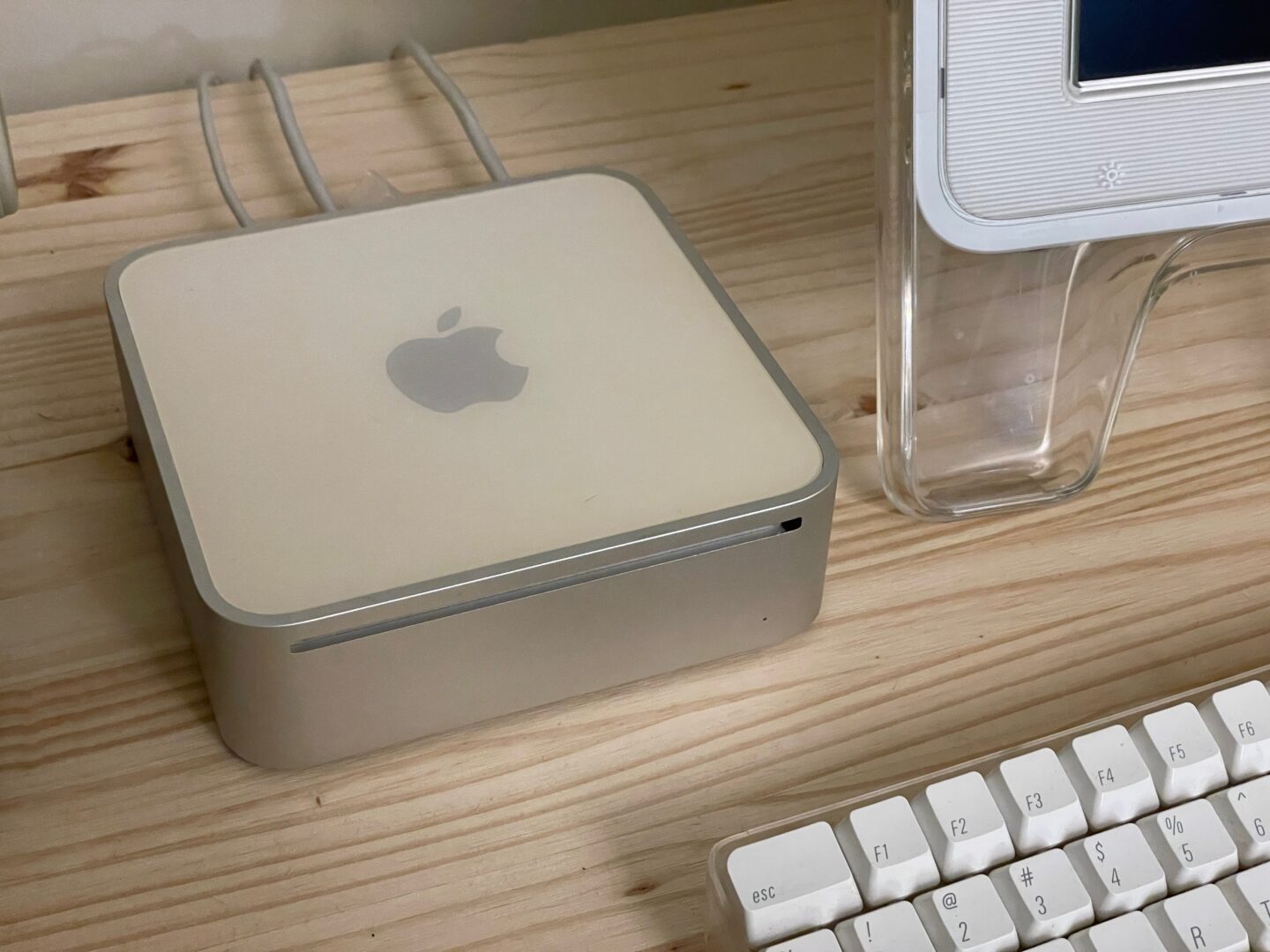 The 2006 Mac mini, old and slightly yellowed, next to the clear acrylic foot of a Cinema Display and the Apple Pro Keyboard.
