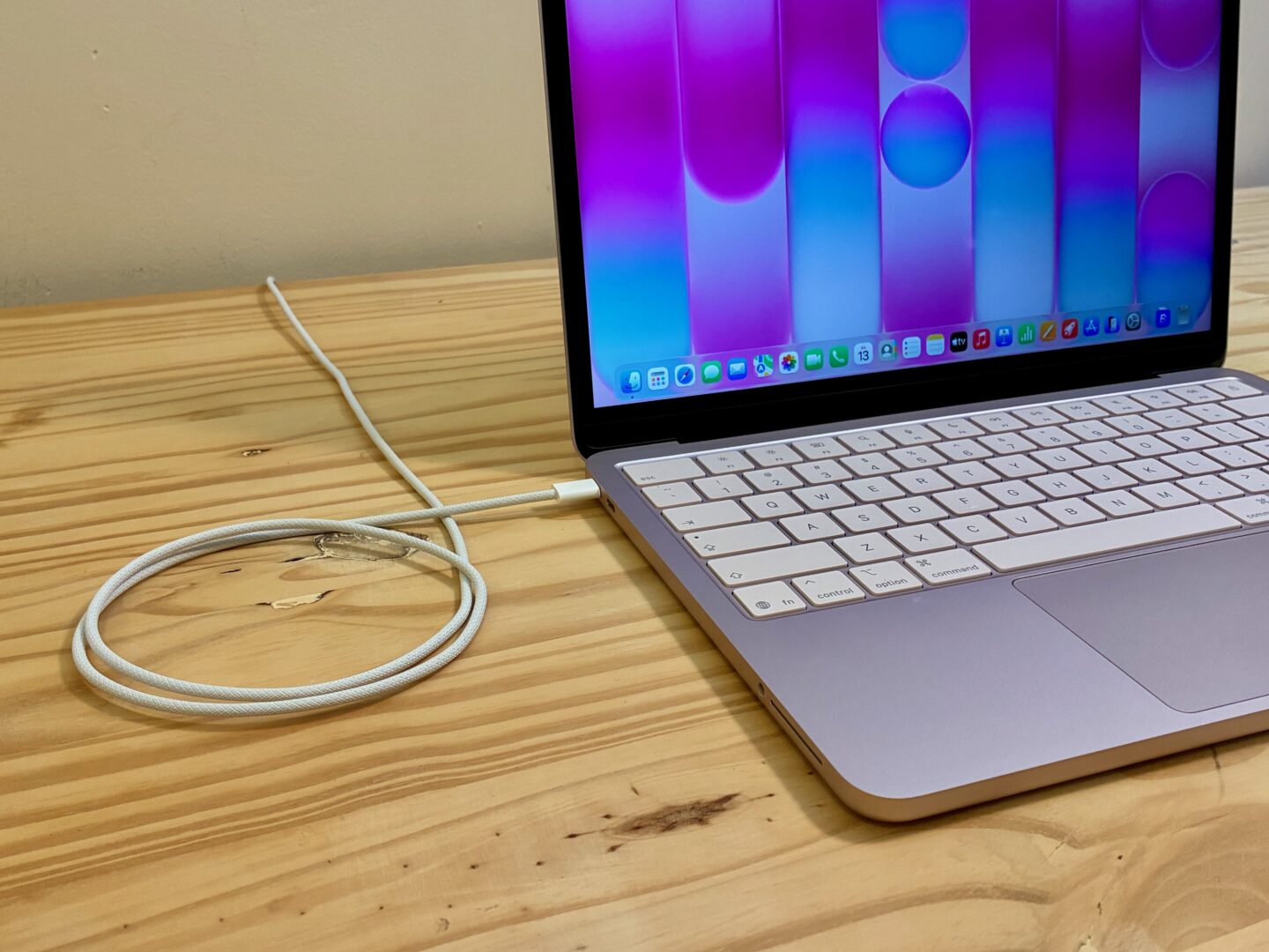 MacBook Neo in Blush charging, with its cable looping around twice.