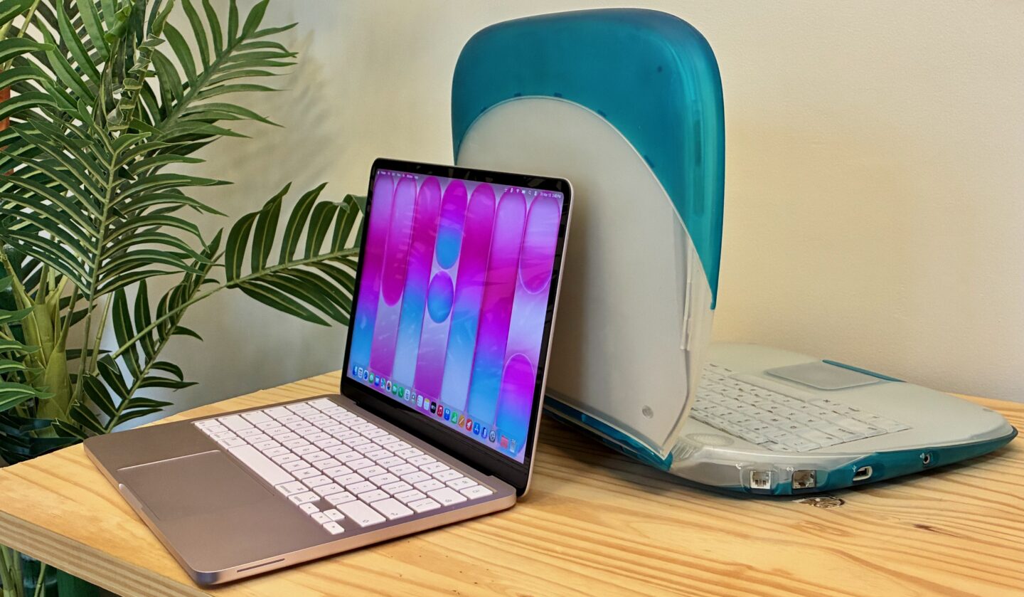 MacBook Neo Blush sitting next to a Blueberry clamshell iBook G3 on a table next to a fake tree