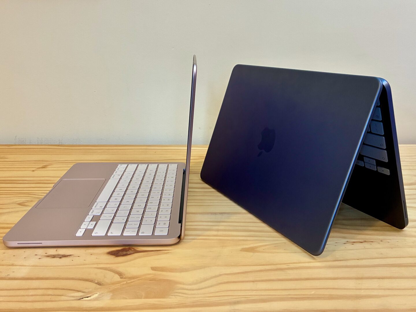 MacBook Neo in Blush and Indigo, one sitting normally, the other folded up and sitting vertically, on a wood table.