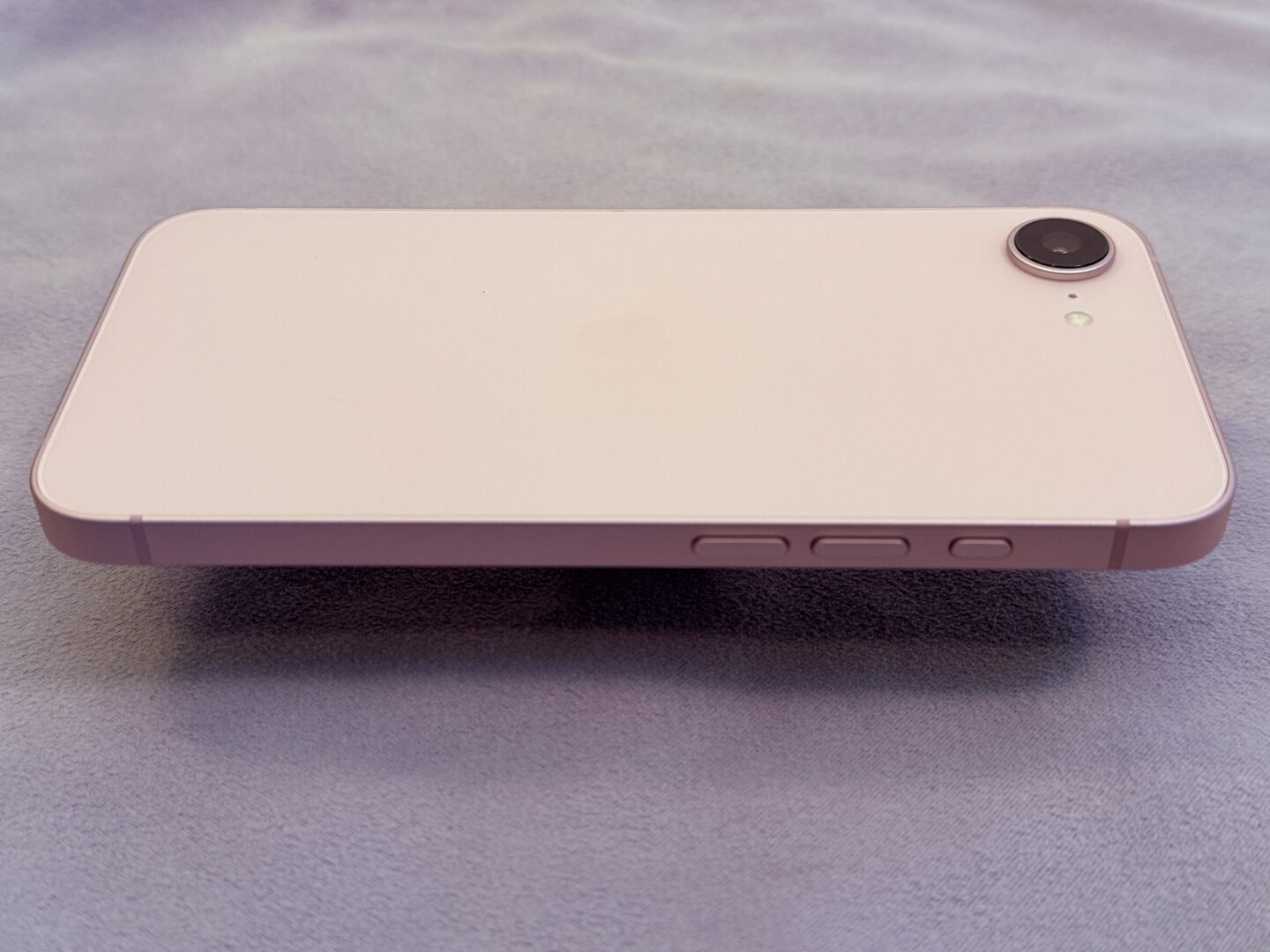 Pink iPhone 17e appearing to float over a gray microfiber cloth