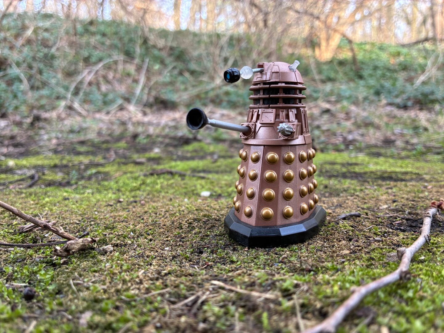 A small toy Dalek from Doctor Who, photographed outside on a patch of moss with a lot of background blur