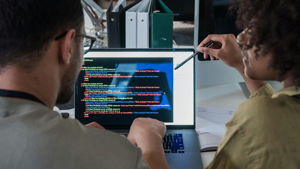 Photo of two people coding on a laptop, used to illustrate a story about Apple employees learning AI coding skills to finish Siri