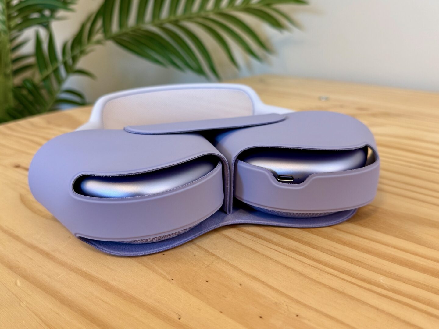 Purple AirPods Max 2 in the case on a pine table in front of a fake palm tree