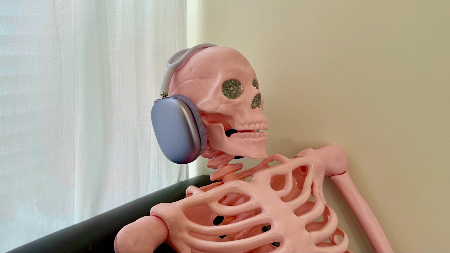 Purple AirPods Max 2 sitting on a pink skeleton with sparkly silver eyes, chilling out on a sofa