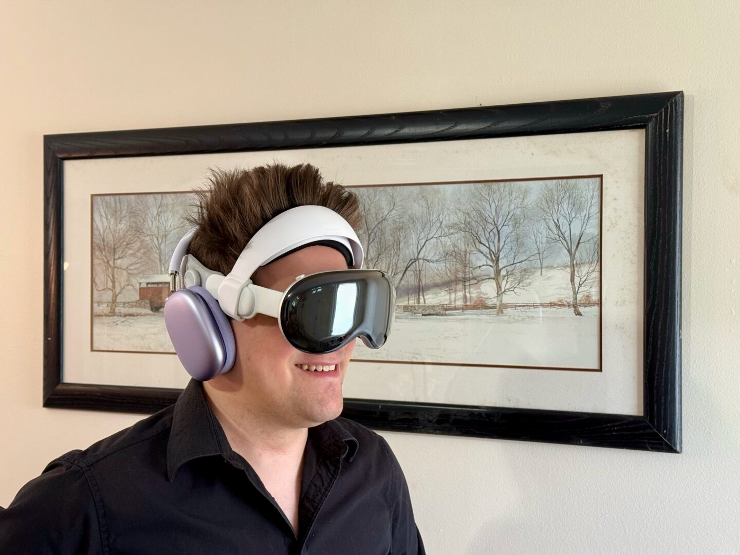 Griffin wearing purple AirPods Max 2 on top of a Vision Pro with the Annapro Top Strap and no Light Seal, looking extremely uncool, despite standing in front of a framed artwork of a covered bridge in winter