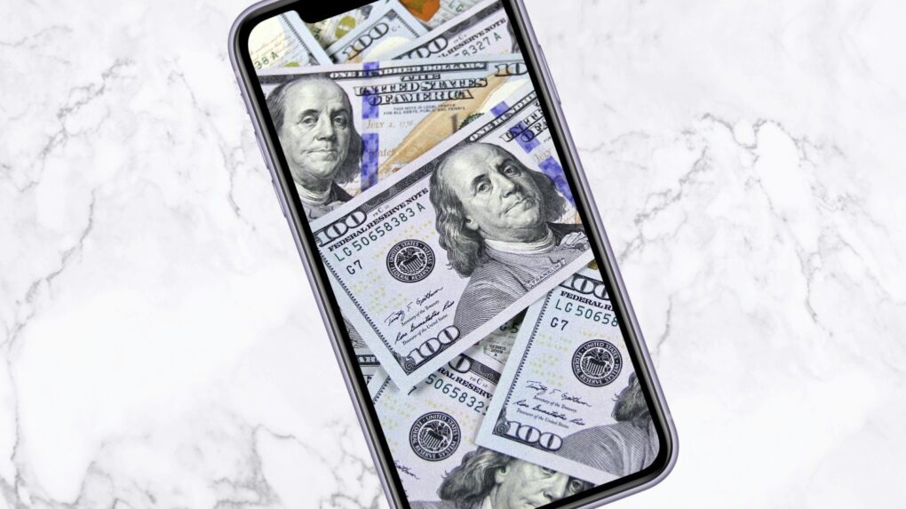 Image of an iPhone with $100 bills on the screen, used to illustrate a story about TSMC's price hikes on processors