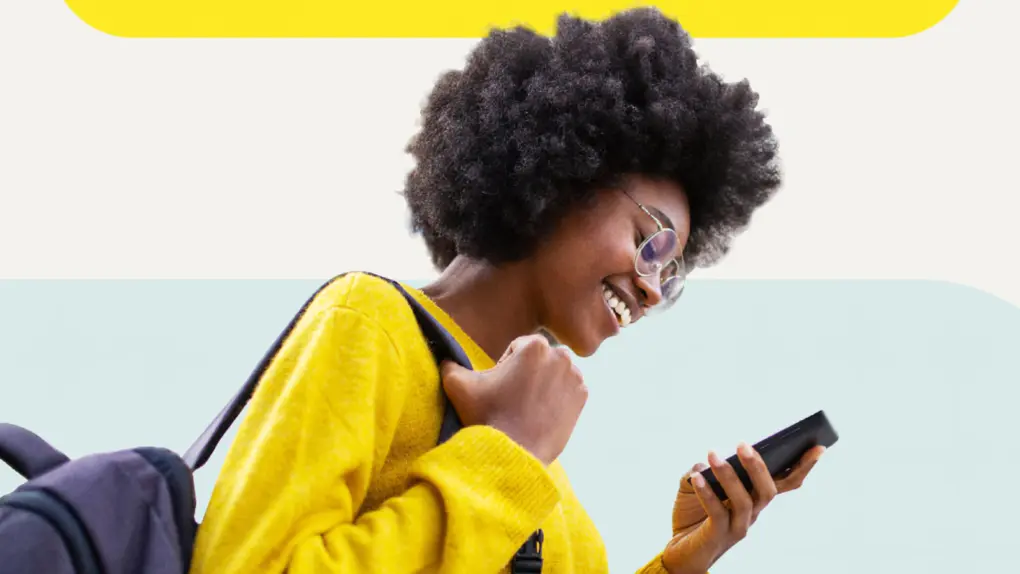 Image of a woman in yellow smiling at the phone she's holding that's running Norton Mobile Security