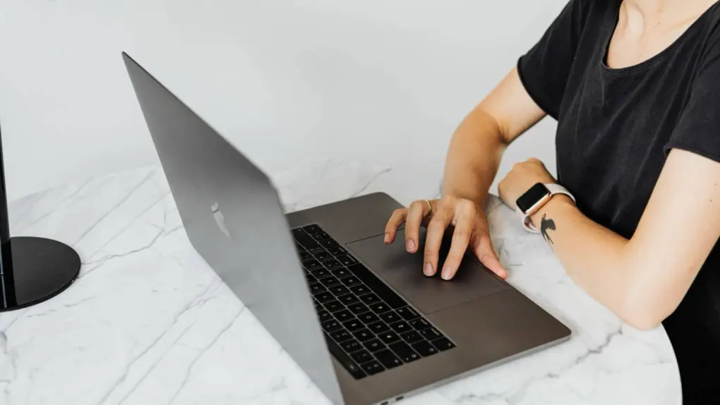 Photo of a woman working with her laptop on a round, marble table while using GhostShield VPN