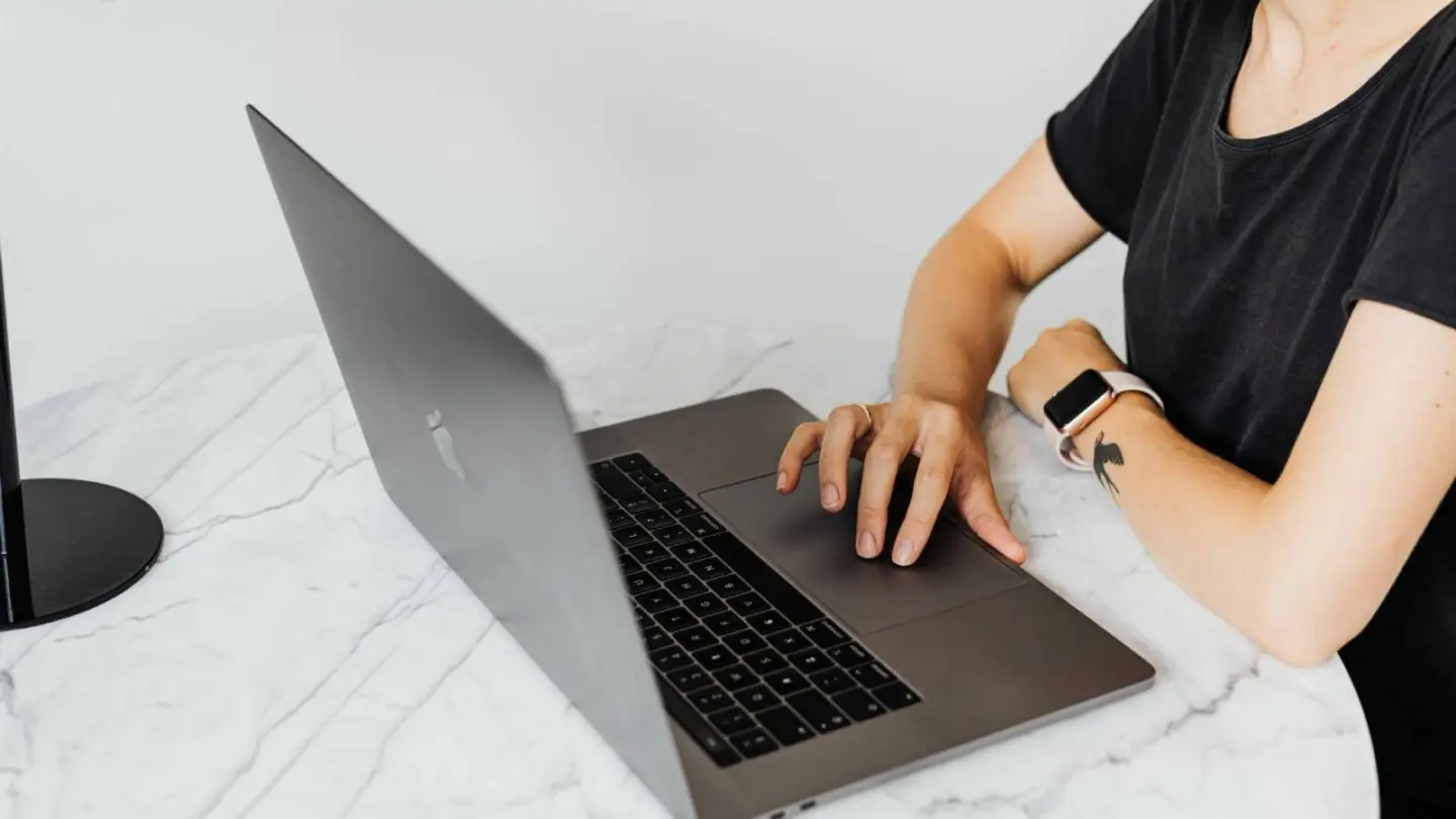 Photo of a woman working with her laptop on a round, marble table while using GhostShield VPN