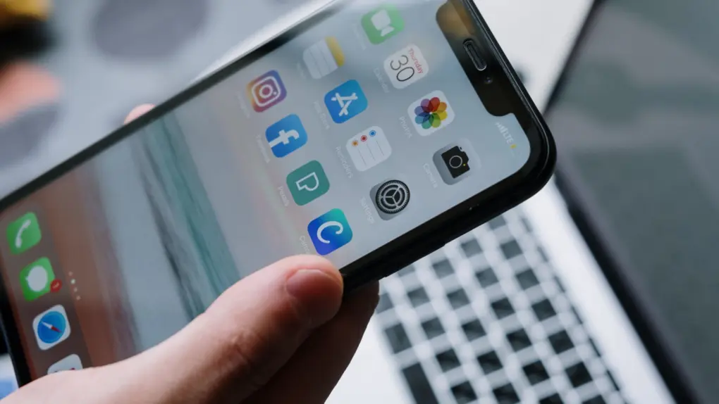 Photo of a hand holding an iPhone with a MacBook keyboard in the background, used to illustrate a post about Swiftspeed AI app builder